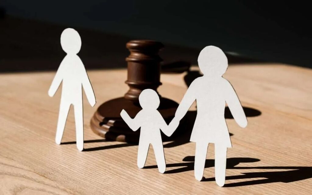 Paper cutout family figures (mother, father, and child) standing near a judge’s gavel, symbolizing family law, child custody, and divorce legal proceedings. Paper cutout family figures (mother, father, and child) standing near a judge’s gavel, symbolizing family law, child custody, and divorce legal proceedings.