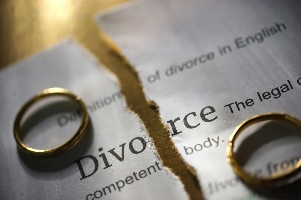Torn divorce document with two wedding rings symbolizing marriage separation, divorce proceedings, and legal relationship breakup.