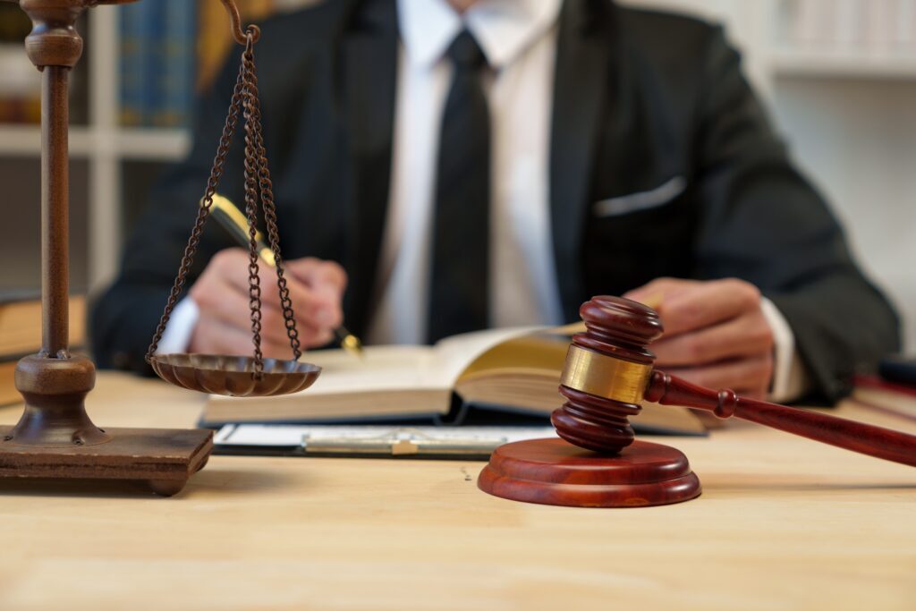 Attorney reviewing legal documents at desk with judge’s gavel and scales of justice, representing courtroom litigation and legal representation. Attorney reviewing legal documents at desk with judge’s gavel and scales of justice, representing courtroom litigation and legal representation.
