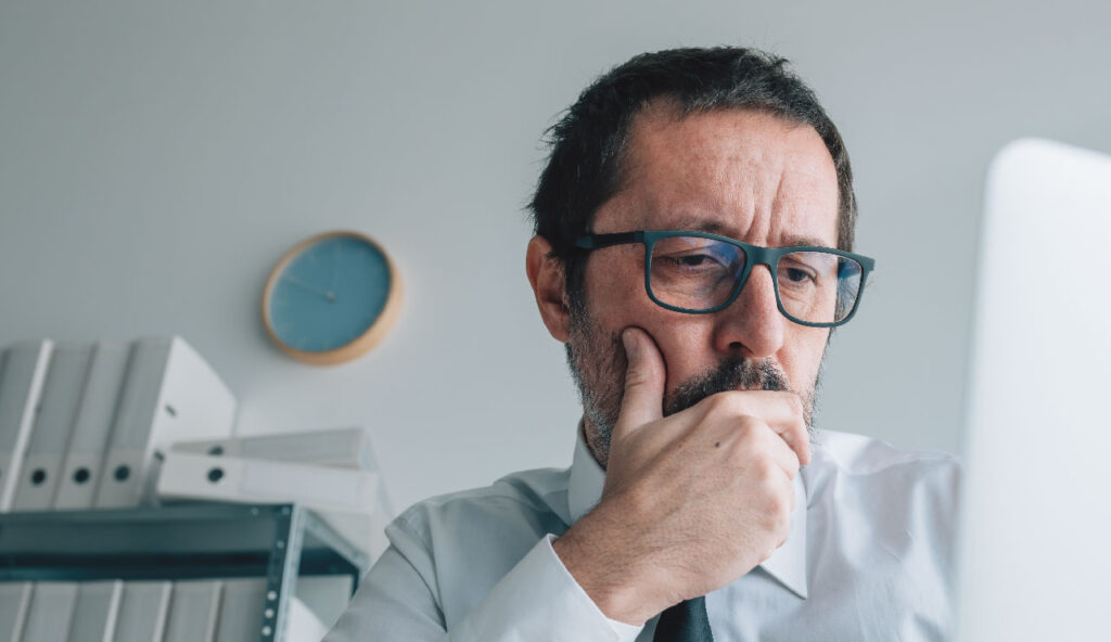 A middle-aged male legal professional with glasses looking thoughtfully at a computer screen in an office setting, representing the diligent case review and strategic planning provided by Wade Litigation.