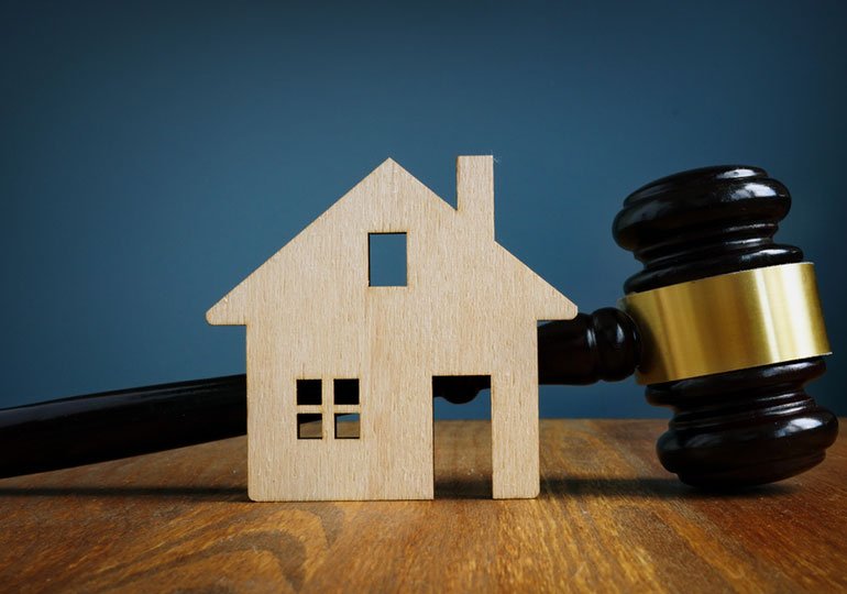 A wooden house model stands in front of a judge’s gavel, symbolizing real estate litigation, property disputes, and court resolution of housing matters.