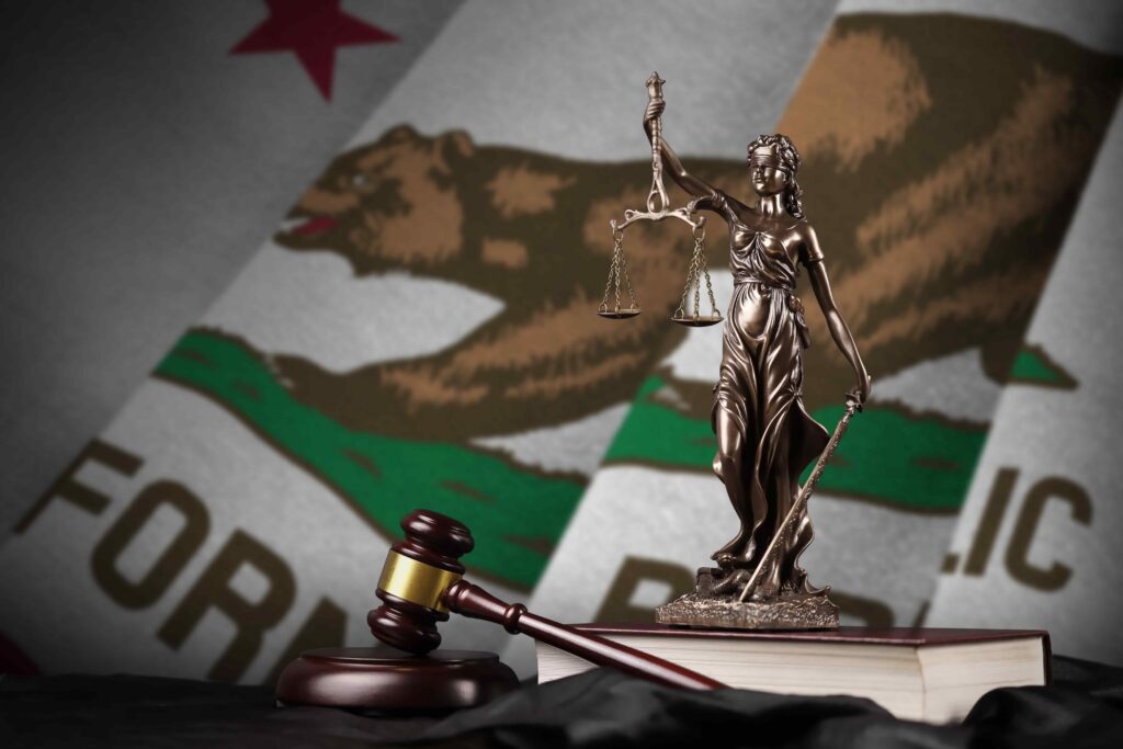 Lady Justice statue and judge&rsquo;s gavel in front of California state flag, symbolizing California courts, state law, and legal system.