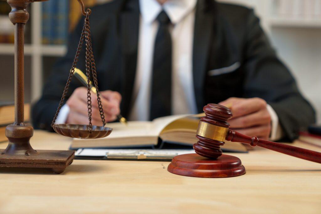 Attorney reviewing legal documents at desk with judge&rsquo;s gavel and scales of justice, representing courtroom litigation and legal representation.