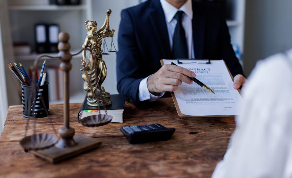 Lawyer reviewing a legal contract with a client at a desk with Lady Justice statue and scales, representing legal consultation and contract agreement.