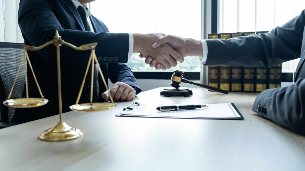 Lawyer and client shaking hands over signed contract with scales of justice and gavel on desk, symbolizing successful legal agreement. Lawyer and client shaking hands over signed contract with scales of justice and gavel on desk, symbolizing successful legal agreement.