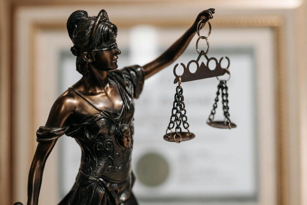 Lady Justice statue holding scales with blurred legal certificate in background, symbol of law, fairness, and justice system Lady Justice statue holding scales with blurred legal certificate in background, symbol of law, fairness, and justice system
