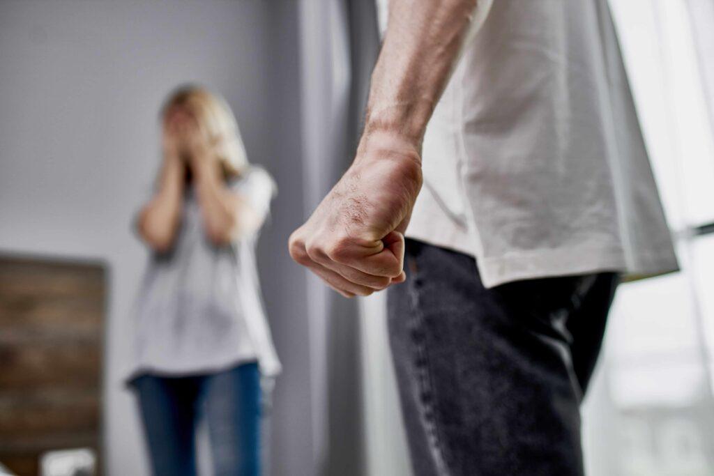 Man with clenched fist in foreground and distressed woman in background, representing domestic violence, abuse, or personal injury situation
