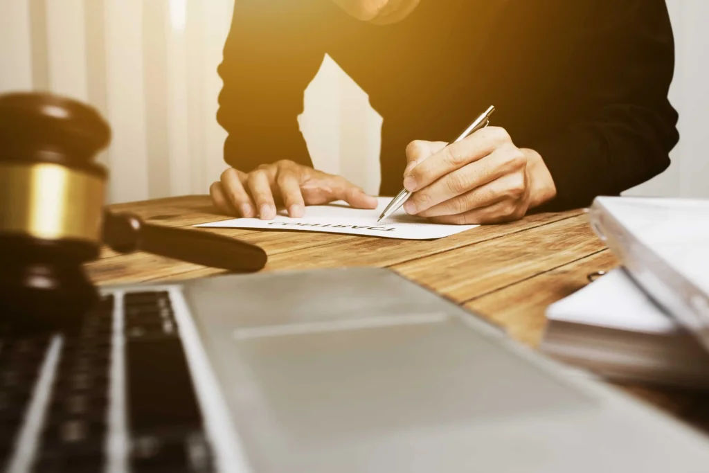 Person signing a legal contract at desk with gavel and laptop, representing legal agreement, attorney services, and contract law