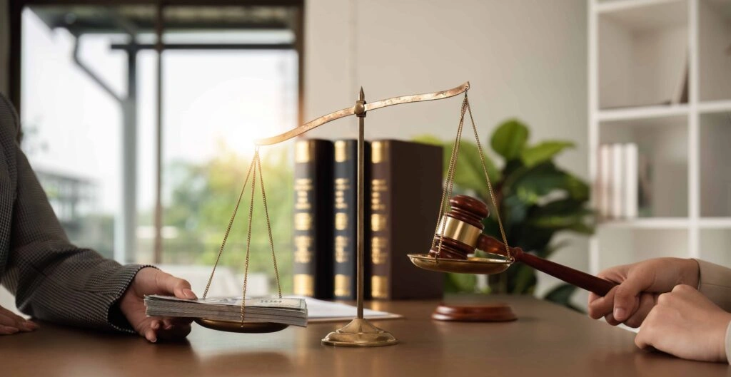 Scales of justice balancing cash and judge’s gavel in law office.