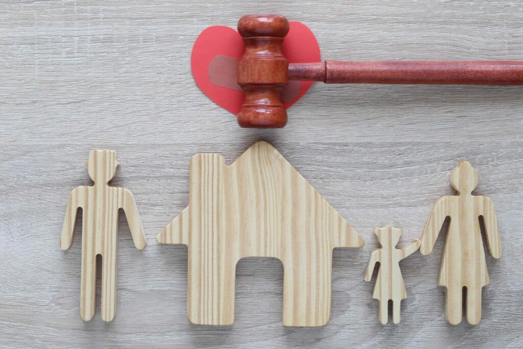 Wooden family figures and house with judge’s gavel on broken heart, symbolizing divorce, child custody, and family law.