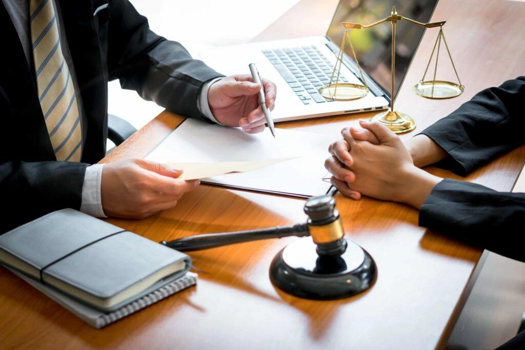 Lawyer discussing legal case with client at office desk, reviewing documents with gavel and scales of justice nearby
