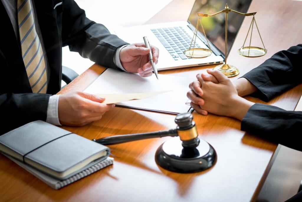 Lawyer discussing legal case with client at office desk, reviewing documents with gavel and scales of justice nearby