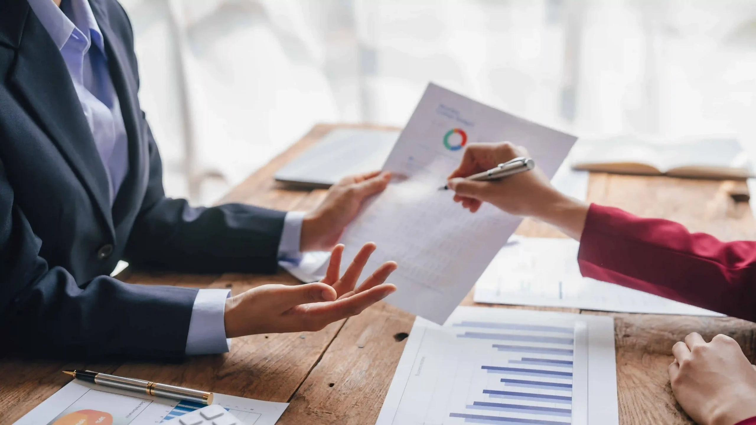 Business professionals reviewing and signing financial documents with charts and reports, representing contract agreement, financial planning, or legal consultation