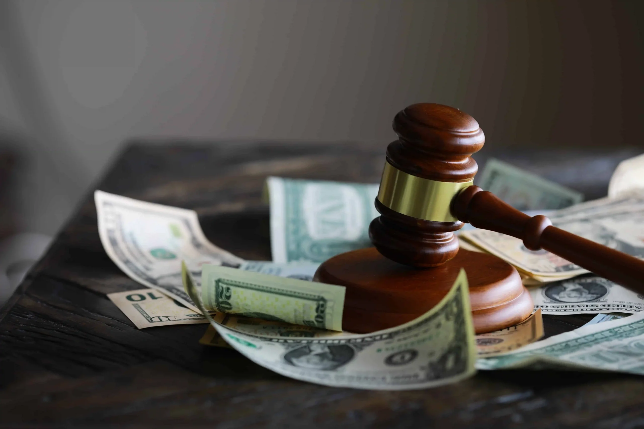 Judge’s gavel resting on US dollar bills, symbolizing legal costs, financial penalties, or lawsuit settlements