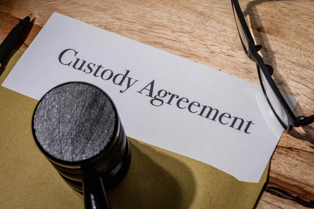 Custody agreement document on desk with judge’s gavel and eyeglasses, representing child custody and family law legal paperwork.